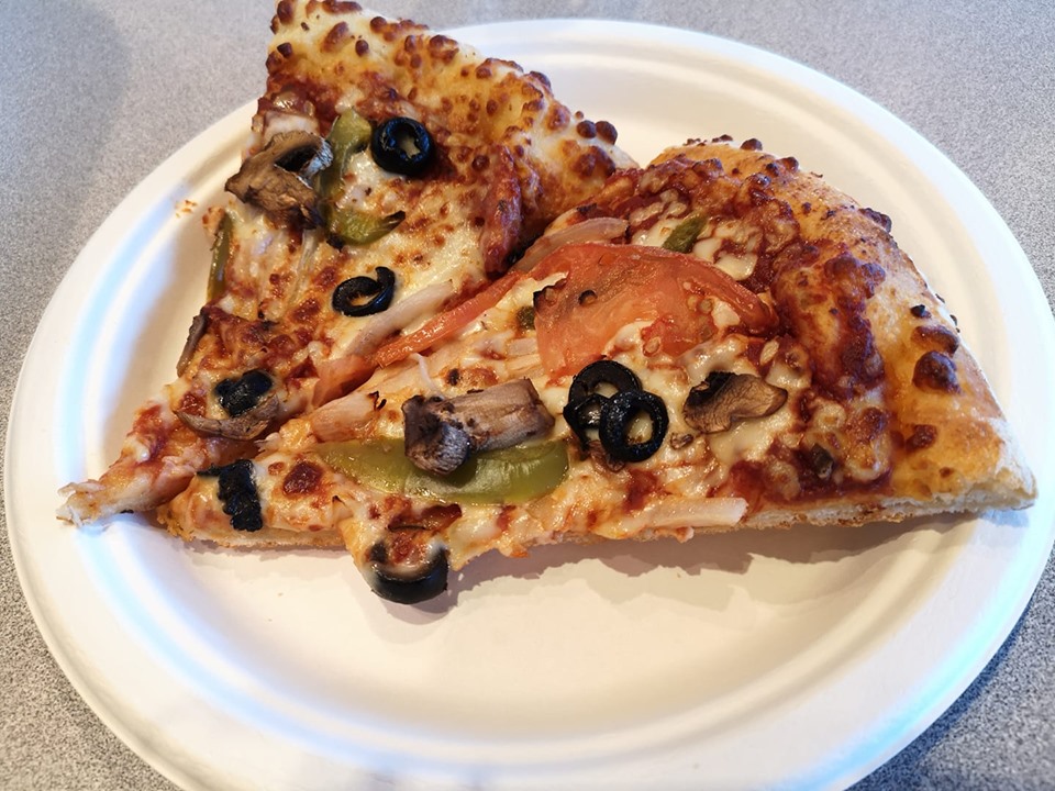 Two slices of deluxe pizza sit on a white paper plate