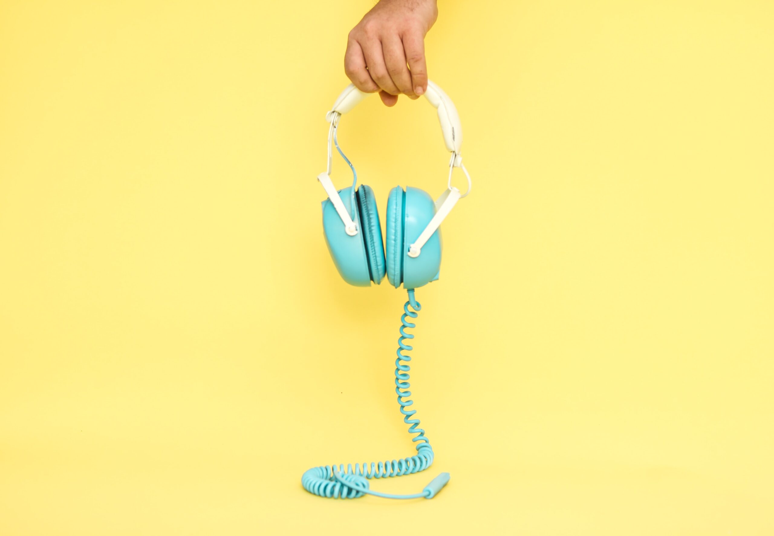 blue headphones held in front of a yellow background