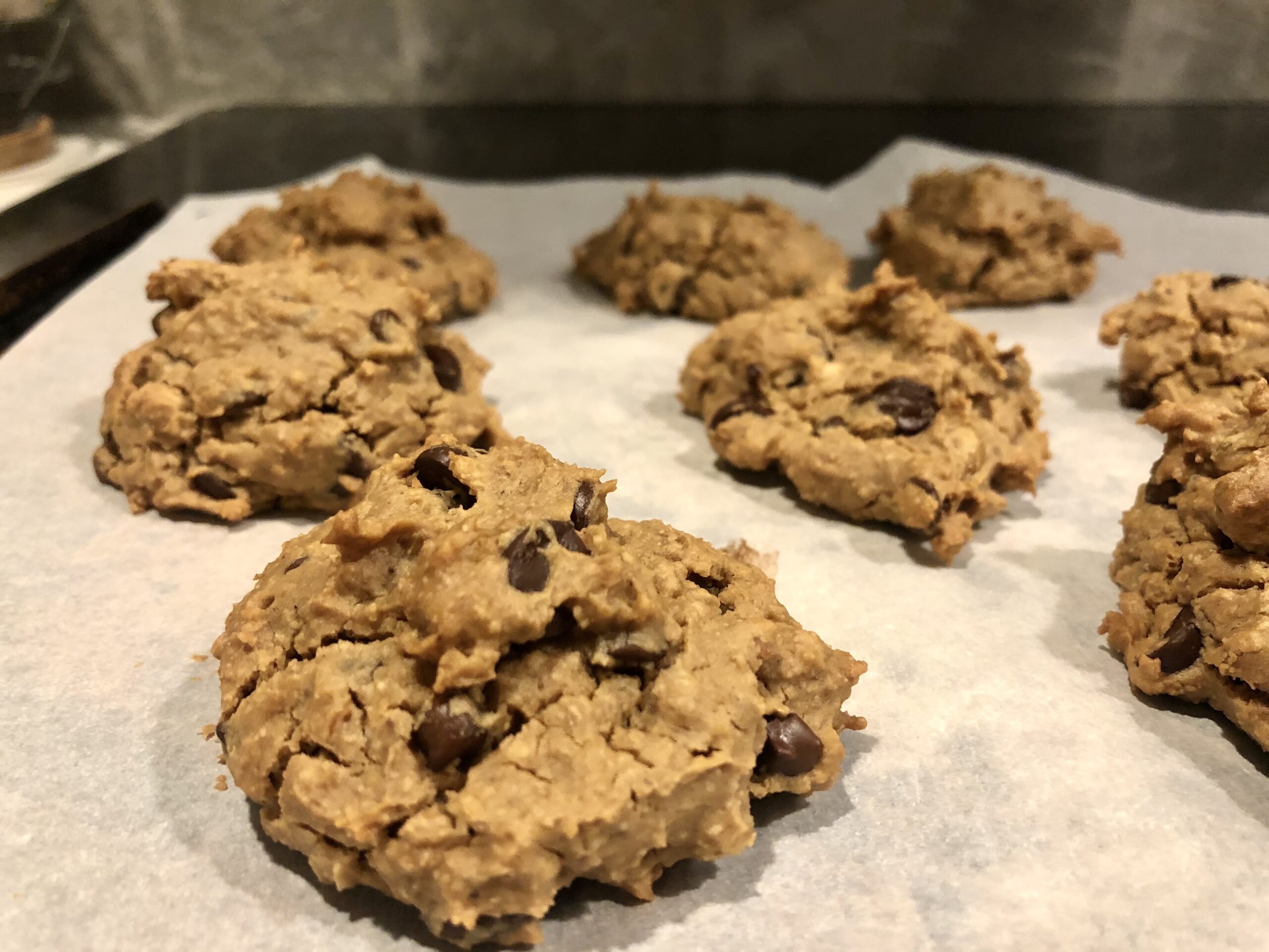 Chocolate chip cookies lying on parchment paper on the stovetop.