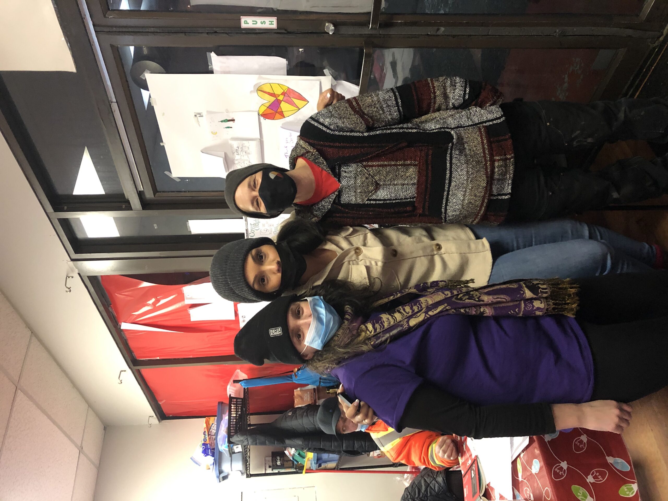 Three Risebridge workers stand beside each other by the main door of the warming centre