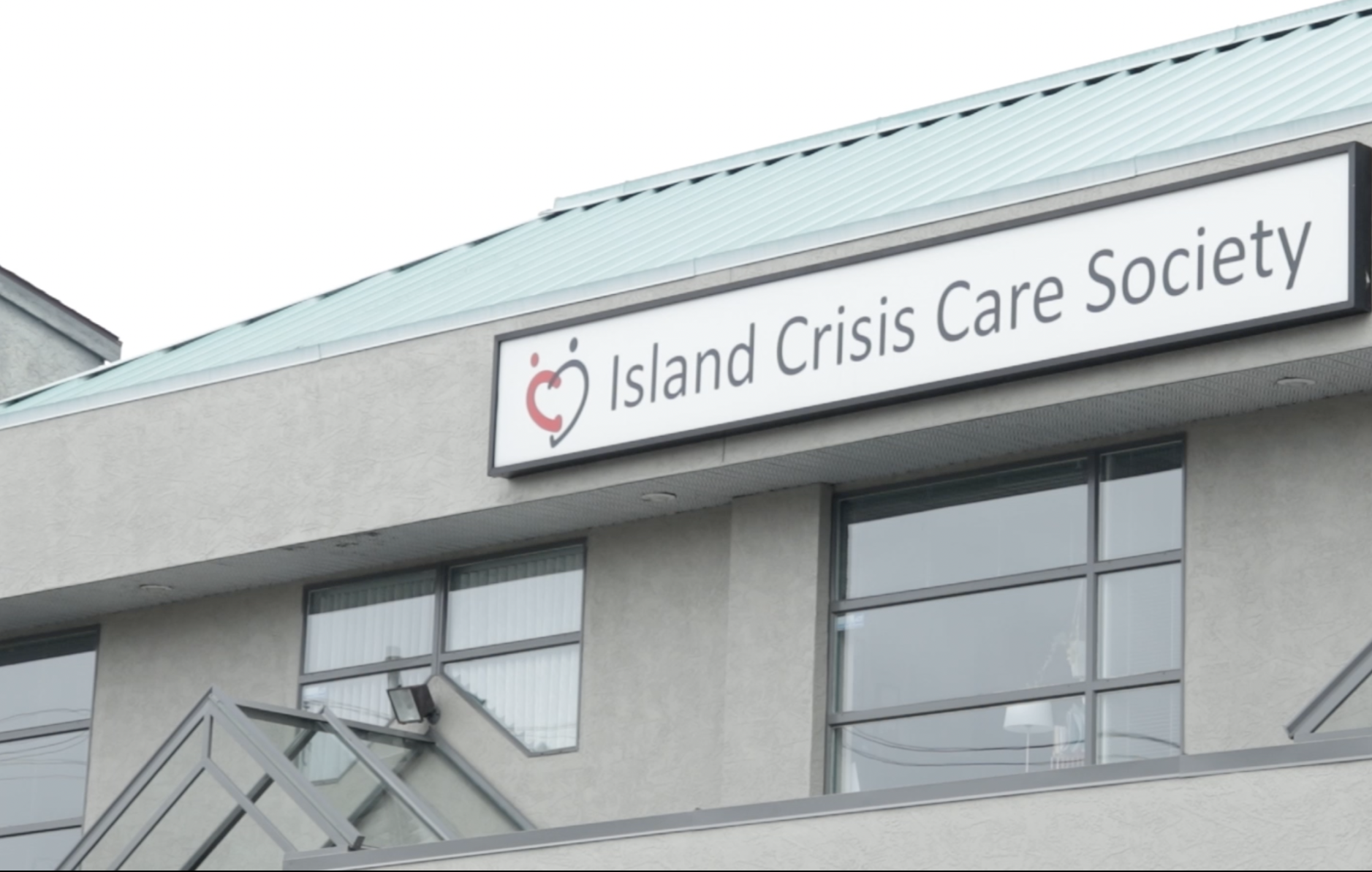 Beige building with green tin roof with sign reading Island Crisis Care