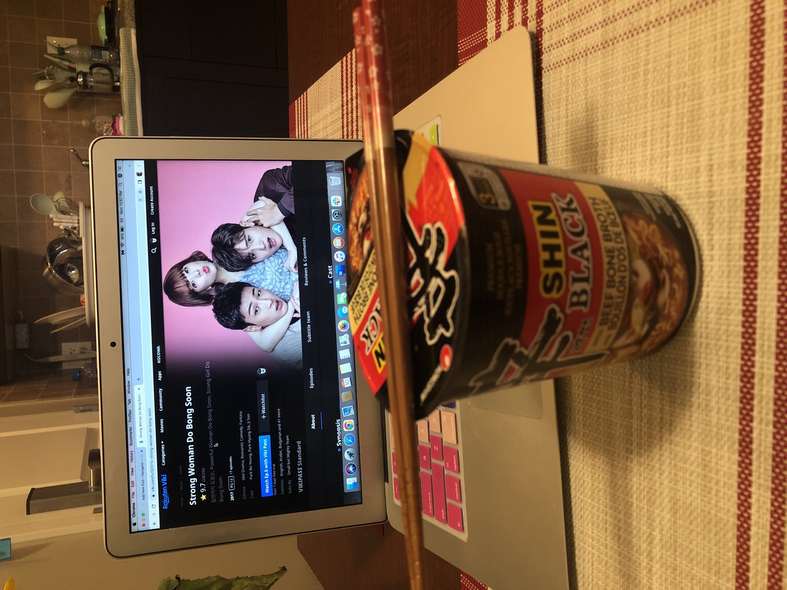 A box of cup ramyun and chopsticks in front of a laptop