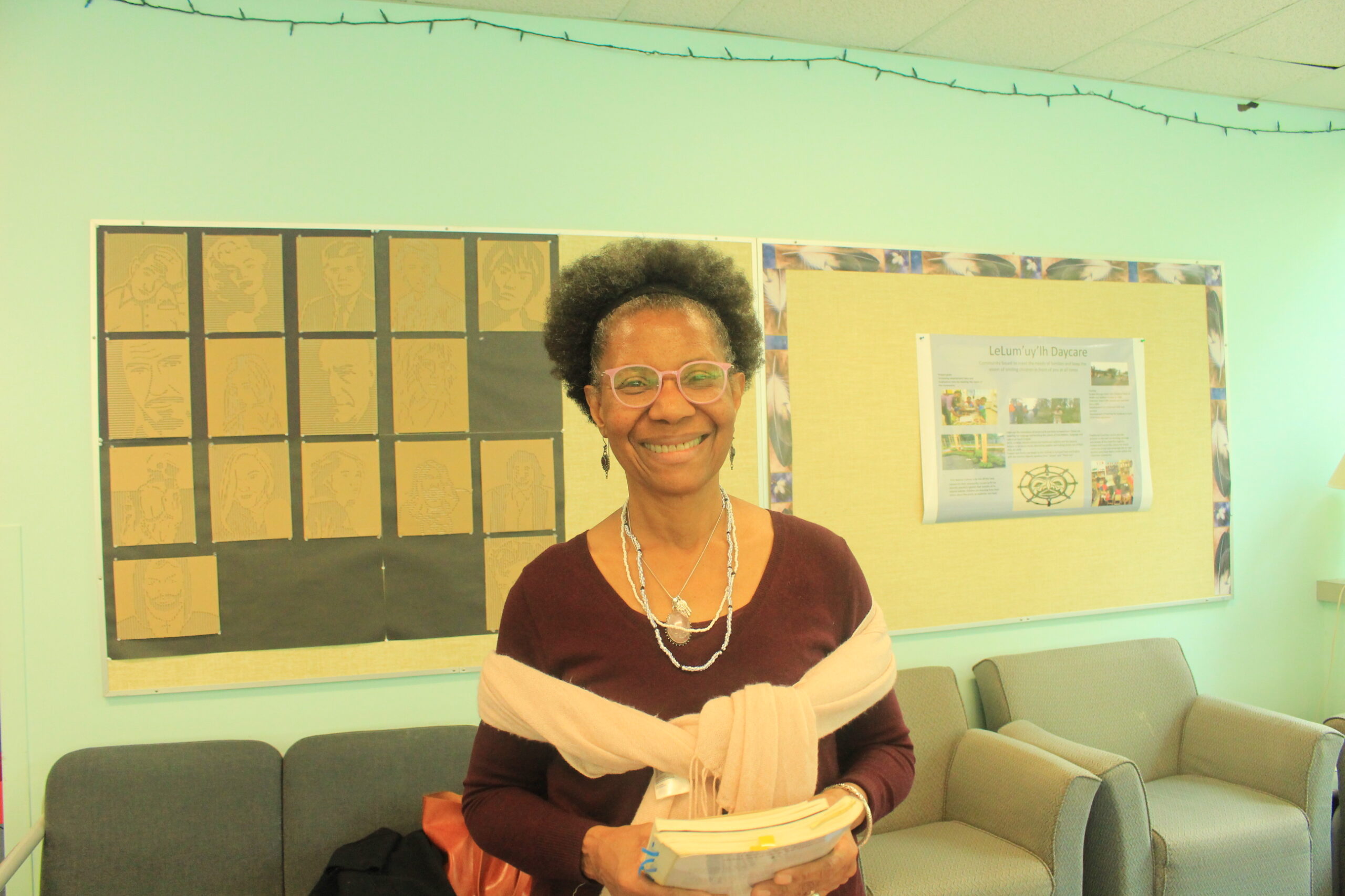 The poet and writer, NourbeSe Philip holding her published books and smiling at the camera. Located in It was in the lounge across from the auditorium (Rm 211) in building 355.