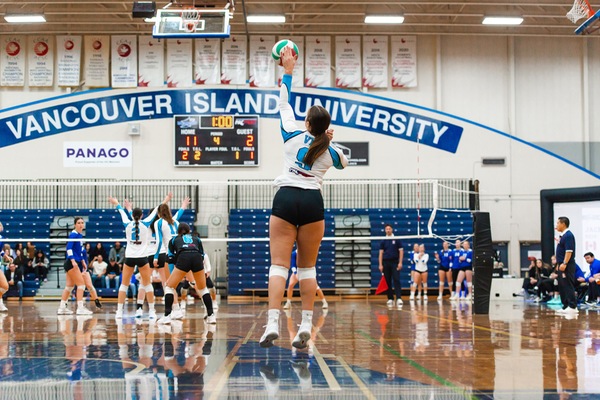 A Mariners volleyball player serves the ball over the net